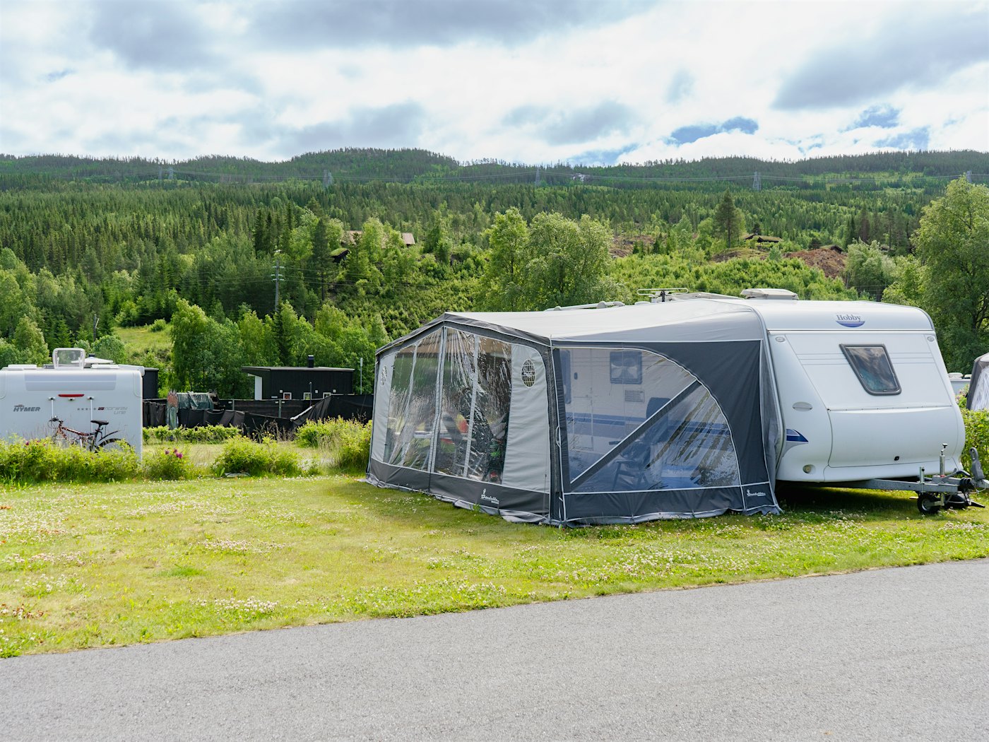 Wohnwagen mit Vorzelt am Campingplatz. Bäume im Hintergrund. Foto