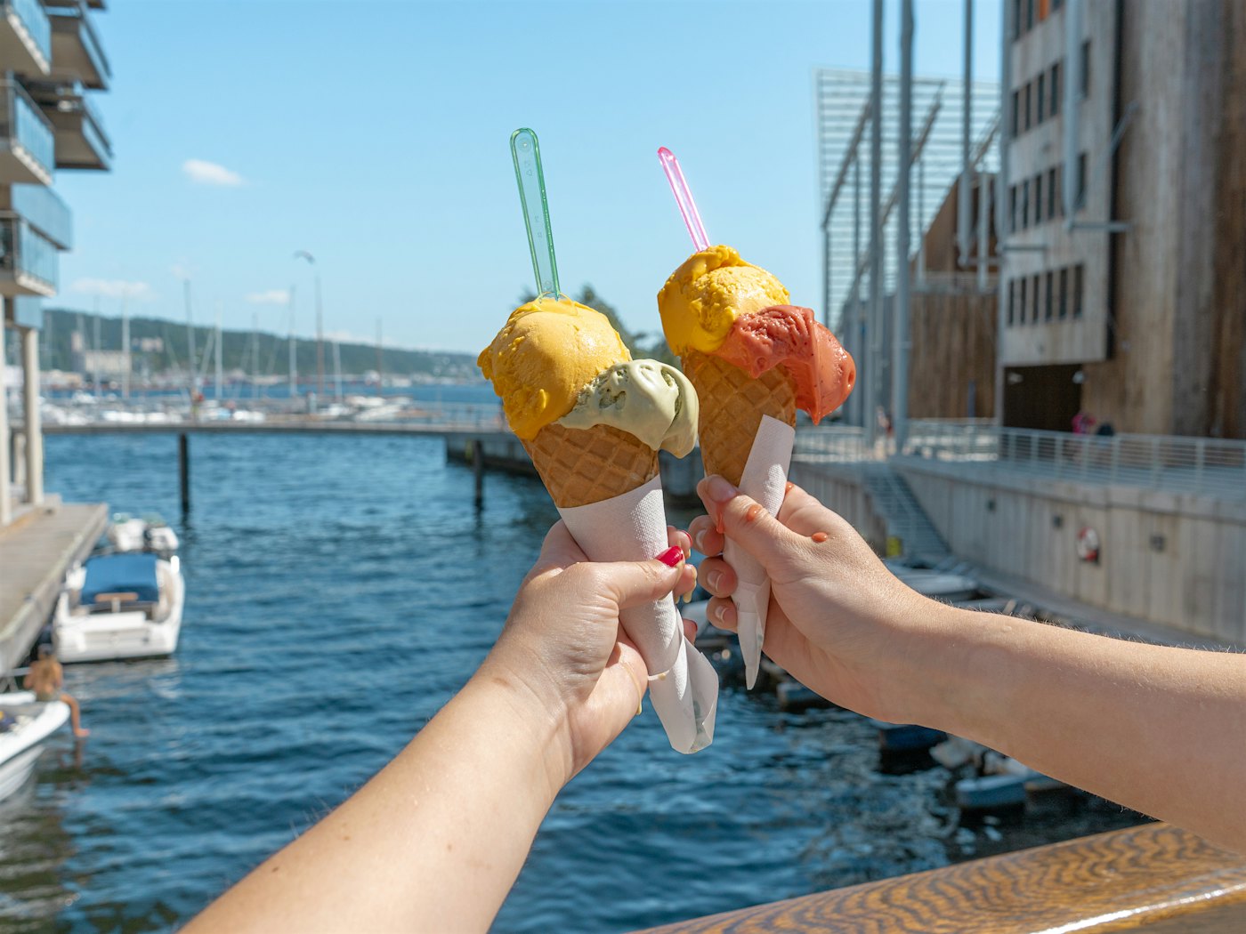 Two arms holding scooped ice cream in a biscuit with two scoops, pier and Tjuvholmen in the background. Photo