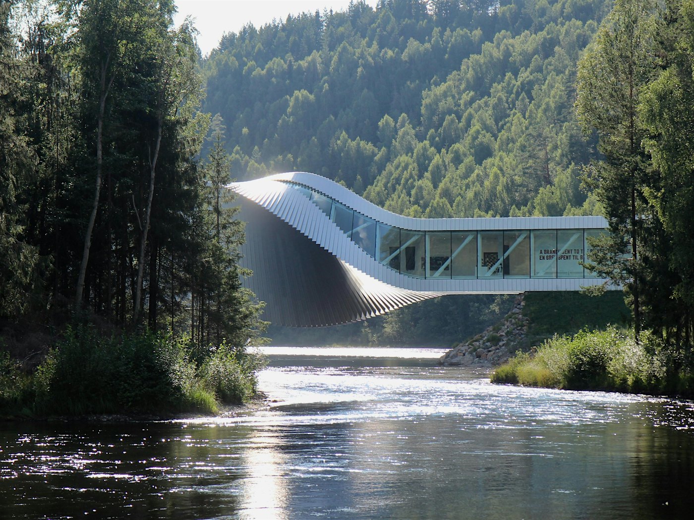 Building with special architecture that stretches over a river, surrounded by forest. Photo