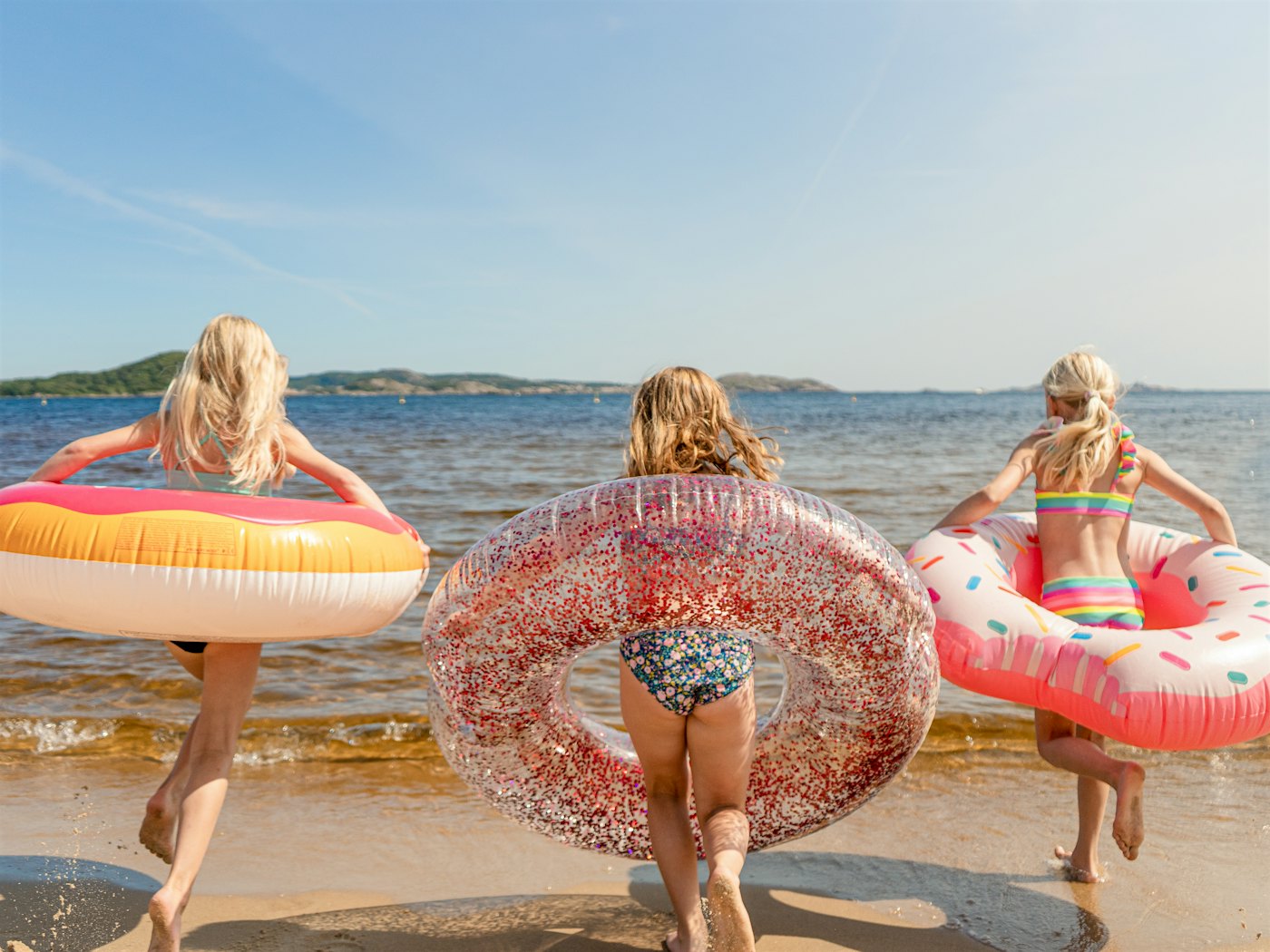 Tre jenter med baderinger koser seg på stranda mens de bader. Foto