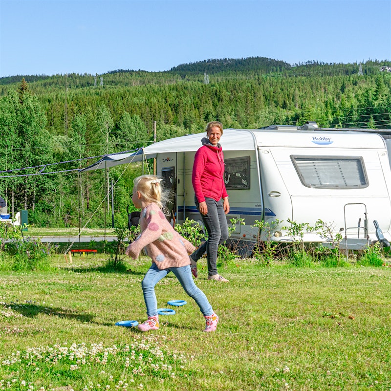 Girl plays at campsite while her mother smiles. Photo