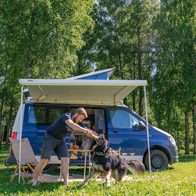Man plays with his dog outside his camper van. Photo