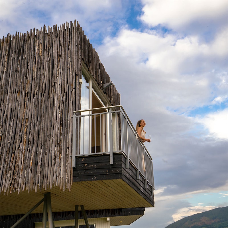 Girl stands on the balcony of a stilt cabin and looks out into the distance. Photo