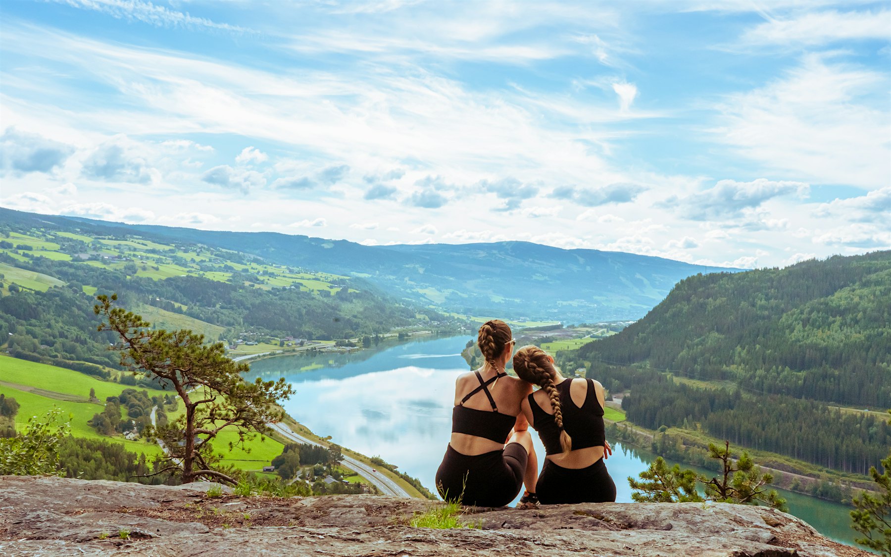 Two girls sit looking at the view from a mountain top. Photo