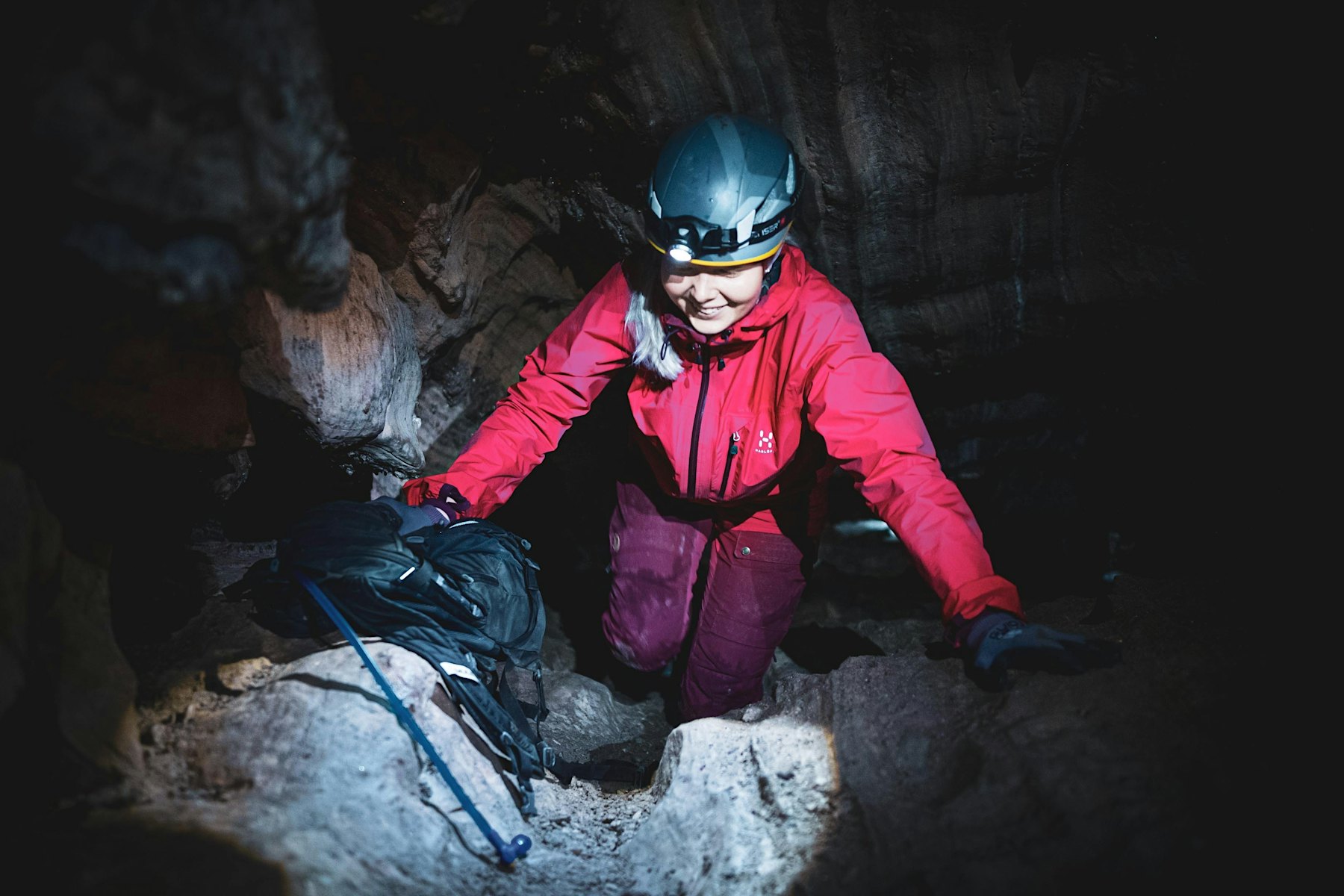 Kvinne utstyrt med hjelm og hodelykt, på vei ned i grotte.