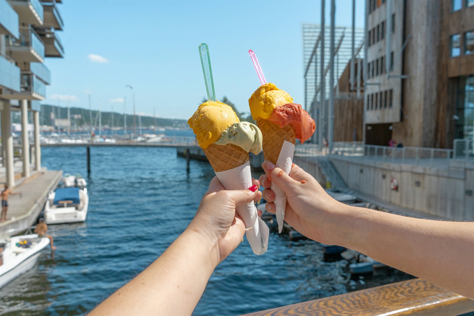 Two arms holding scooped ice cream in a biscuit with two scoops, pier and Tjuvholmen in the background. Photo