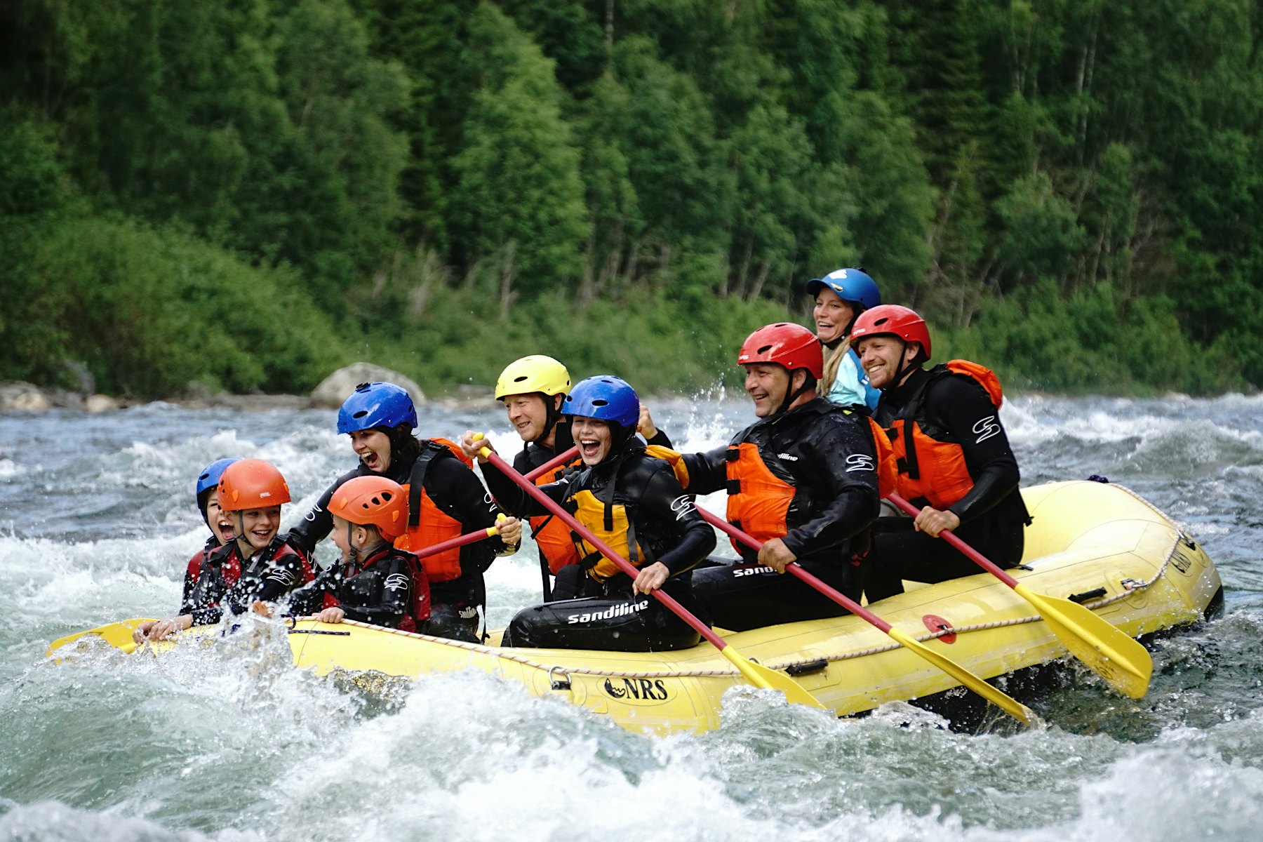 Große Gruppe, die in einem Boot sitzt und in einem Fluss raftet, während sie lacht und lächelt. Foto