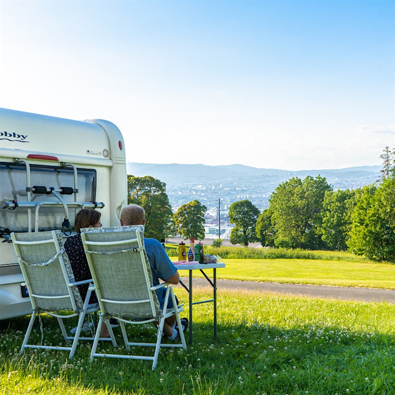 A couple sits outside their caravan eating dinner while looking at the view. Photo