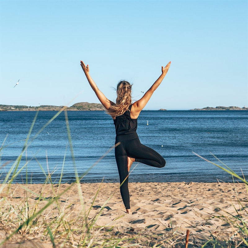 Frau macht Yoga-Pose am Strand und blickt aufs Meer. Foto