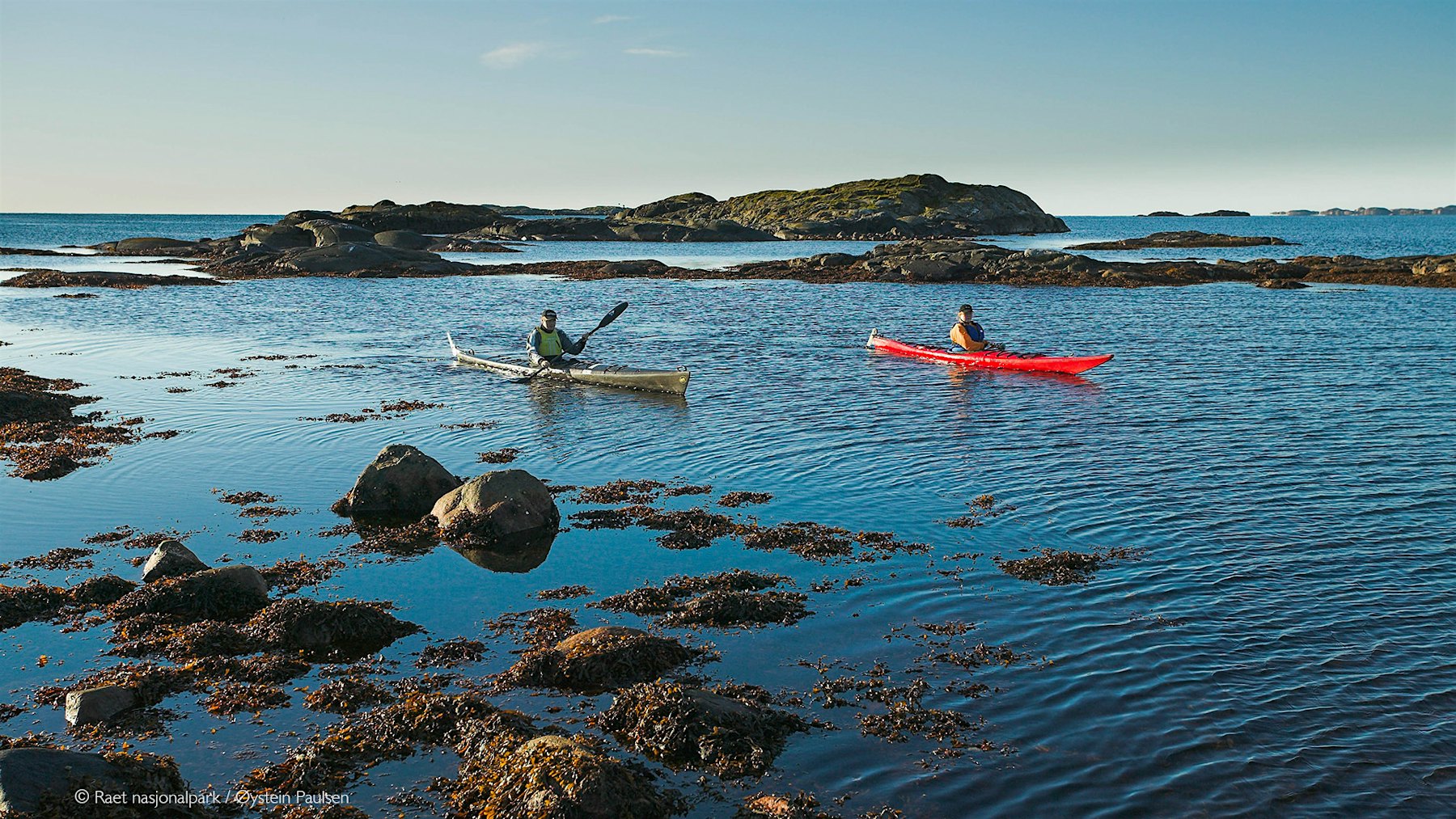 Two kayakers on the sea, with rocky cliffs around. Photo