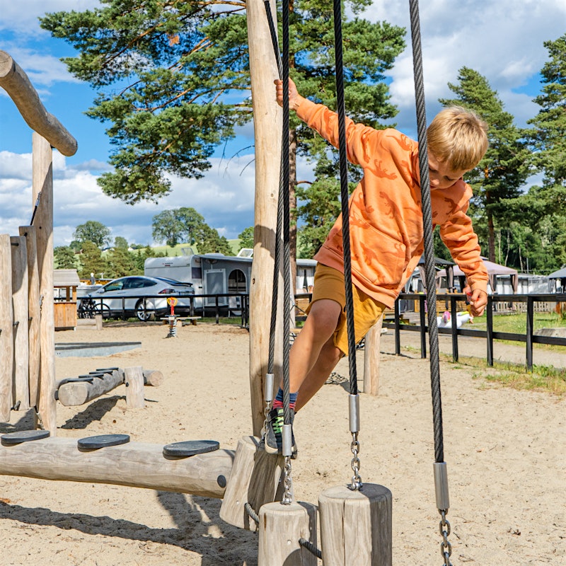 Gutt balanserer mellom trestopler på lekepark på stranda.