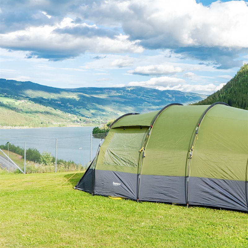 Telt står oppstilt på gressplen med utsikt over fjell og vann.