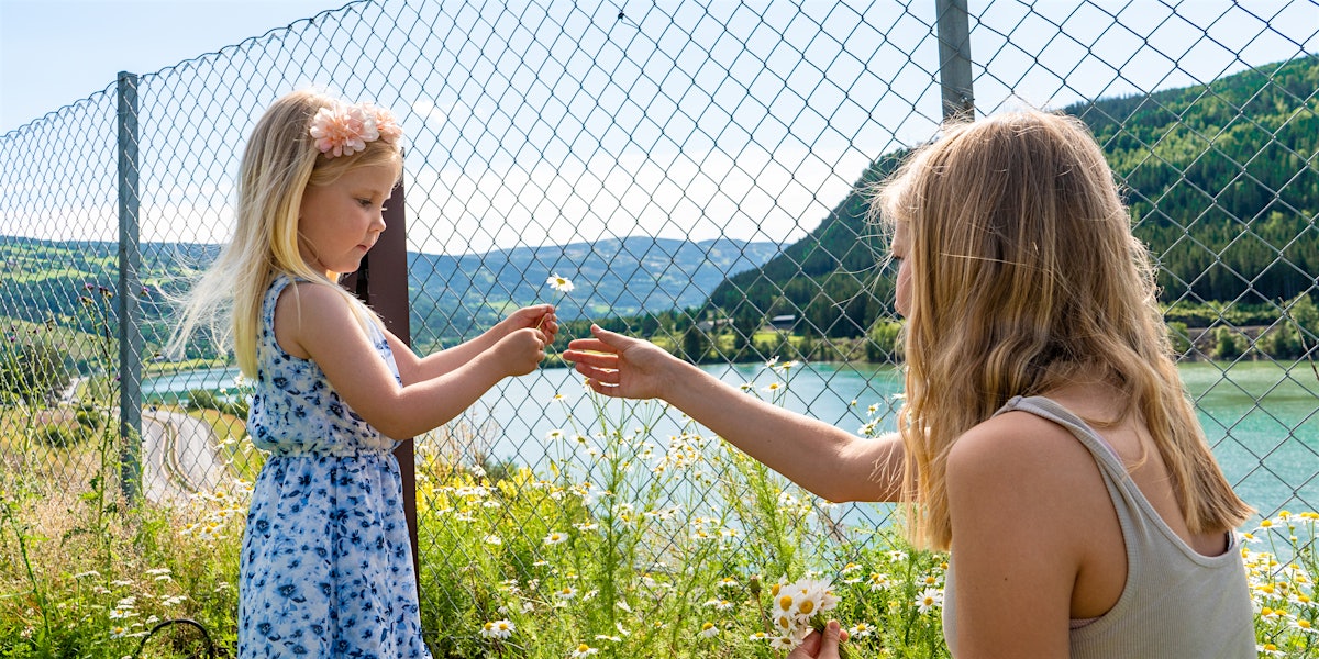 Two sisters pick flowers with a view of Gudbrandsdalslågen. Photo