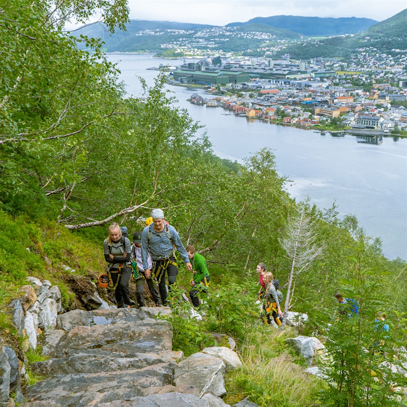 A group goes up the Helgeland steps with climbing equipment, with Mosjøen in the background. Photo