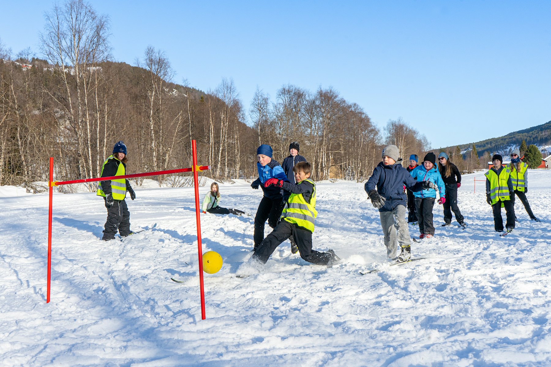Barn løper etter fotball med ski på beina. Foto