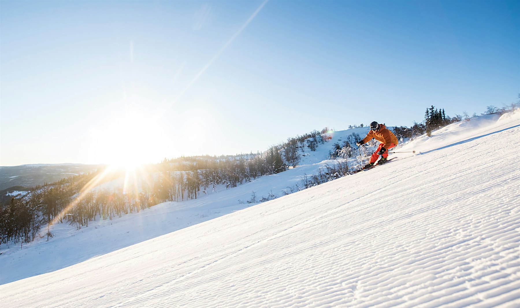 Alpinist i oransje klær i full fart på ski nedover Ål Skisenter med sola i bakgrunn