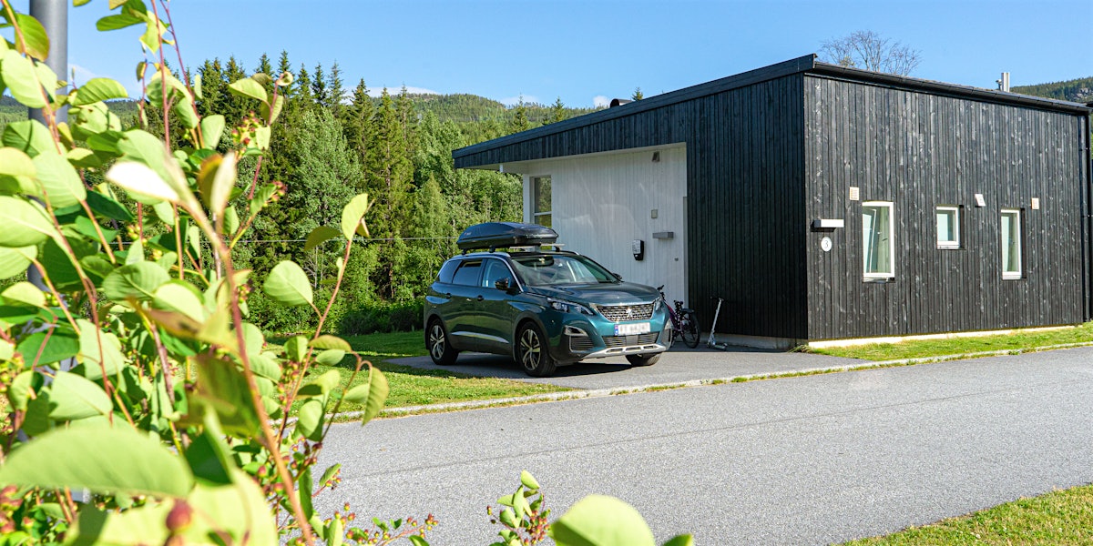 Car is parked outside the cabin, with green plants in the foreground. Photo