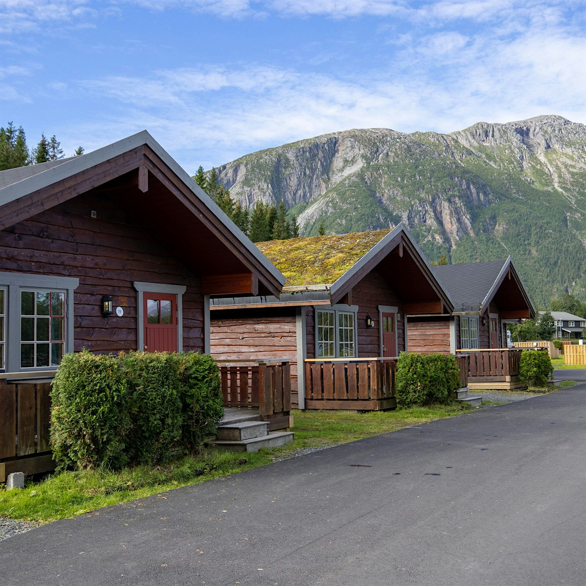 Three log cabins with grass on the roof and green lawn around, with mountains in the background. Photo