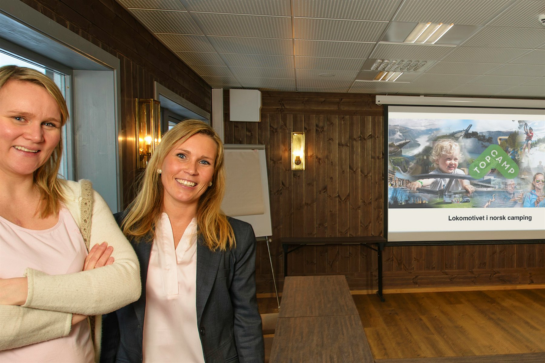 To kvinner står Stallen konferansesal på Topcamp Hallingdal og smiler til kamera. Foto