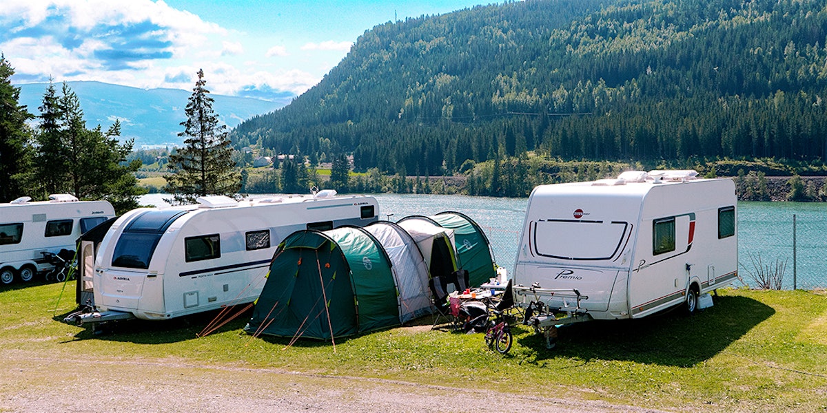 two caravans with a tent in between are on the campsite next to the water