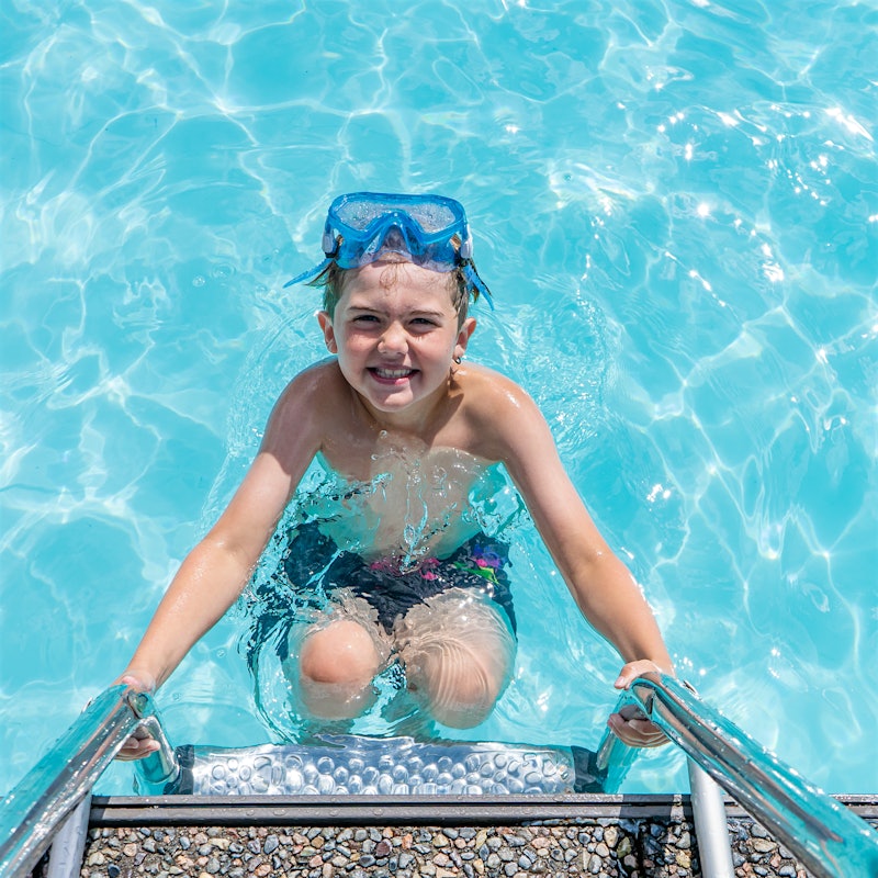 Junge mit Schnorchel lächelt breit, während er an der Leiter im Pool hängt. Foto