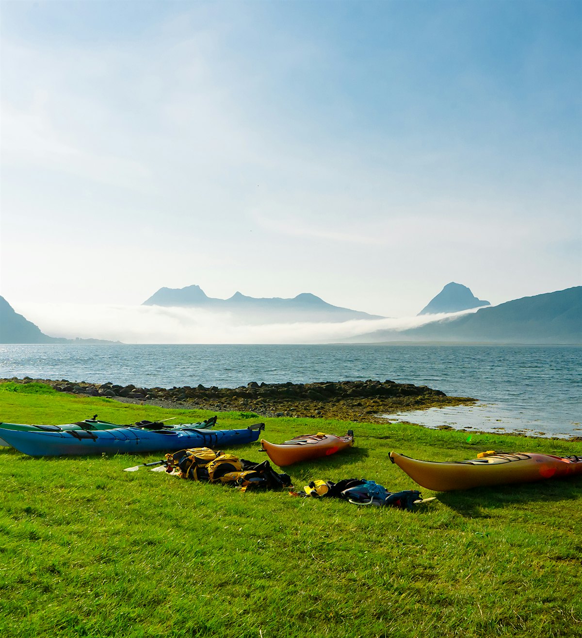 Kayaks lie on the shoreline with mountains in the background. Photo